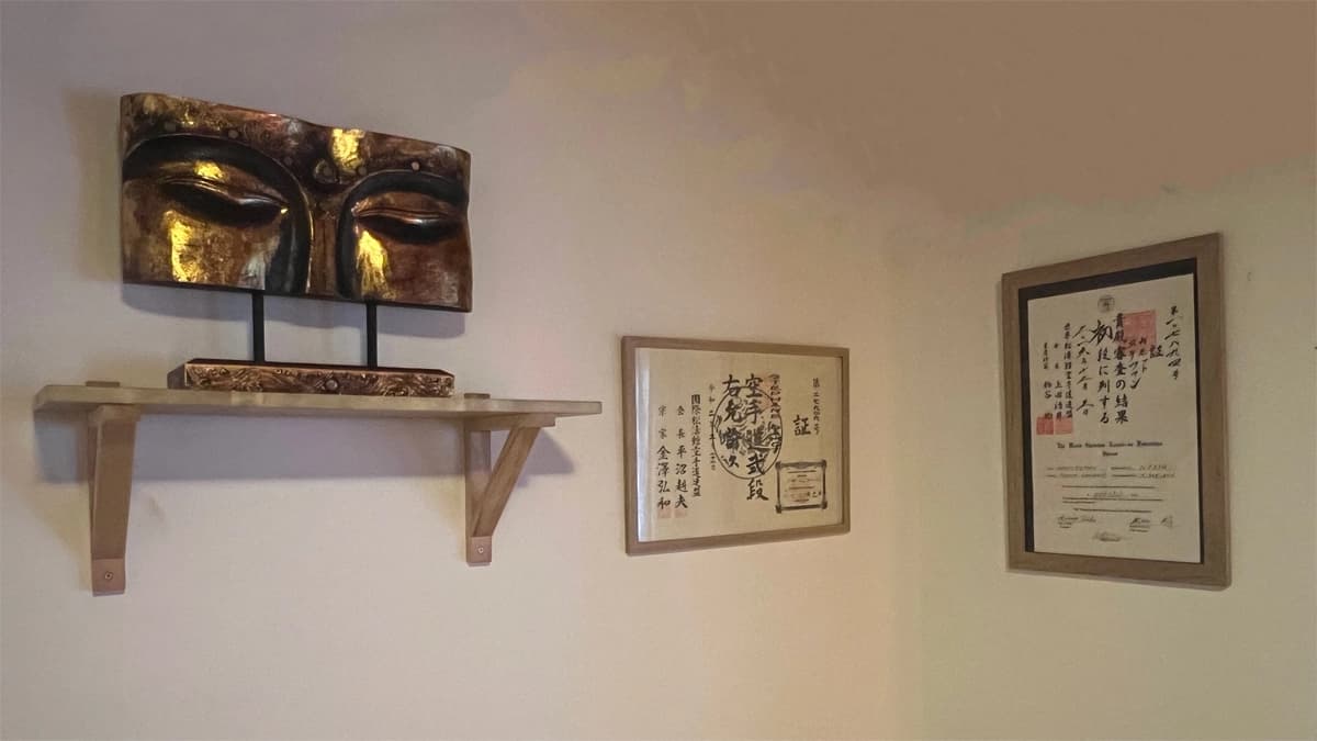 Gros plan sur les yeux d’un Bouddha avec deux diplômes japonais de shiatsu exposés à côté